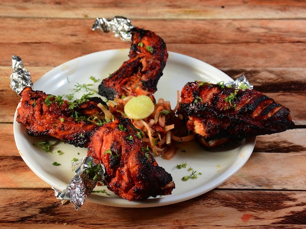 Tandoori chicken prepared by roasting chicken marinated in yoghurt and spices in a tandoor served over a wooden rustic background selective focus