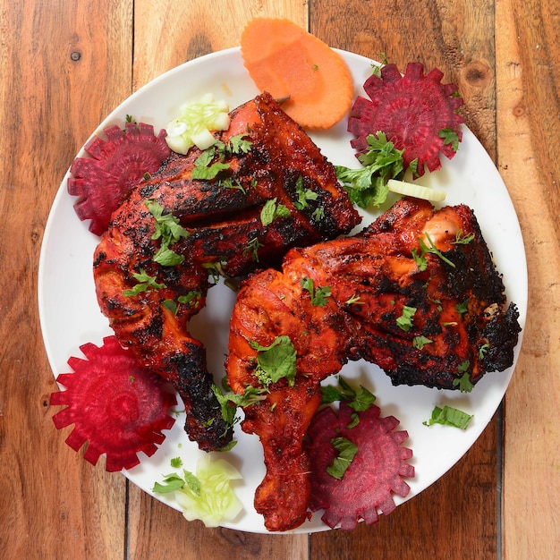 Tandoori chicken prepared by roasting chicken marinated in yoghurt and spices in a tandoor served over a wooden rustic background selective focus