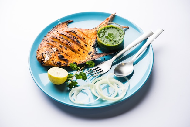 Tandoori Pomfret fish cooked in a clay oven and garnished with lemon , mint, cabbage and carrot salad. Selective focus