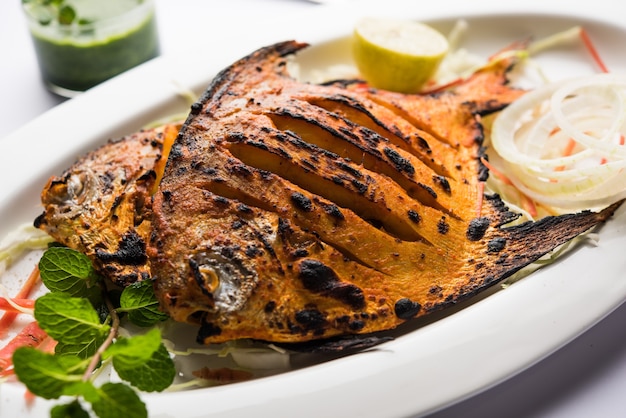 Tandoori Pomfret fish cooked in a clay oven and garnished with lemon , mint, cabbage and carrot salad