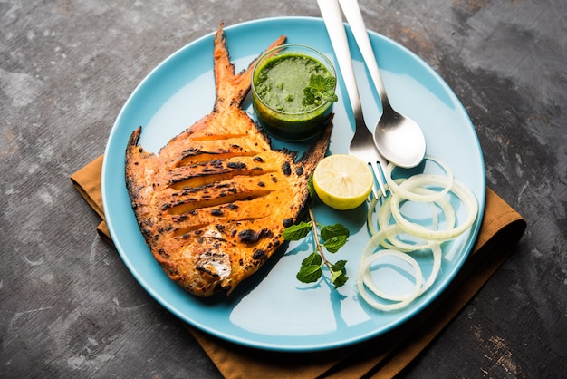 Photo tandoori pomfret fish cooked in a clay oven and garnished with lemon , mint, cabbage and carrot salad