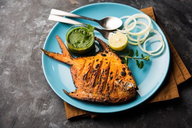 Photo tandoori pomfret fish cooked in a clay oven and garnished with lemon , mint, cabbage and carrot salad