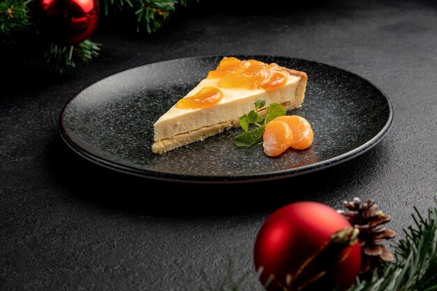 Tangerine dessert garnished with tangerine wedges and mint, served on a black plate. dish on black christmas background