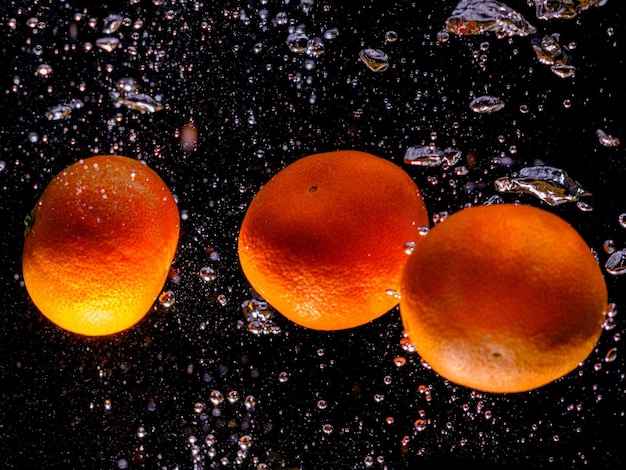 Tangerines falling into water with splash on black background