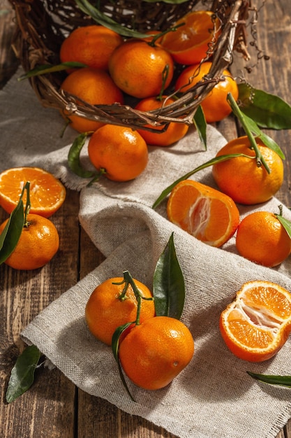 Tangerines falling out of the basket. Oranges, mandarins, clementines, citrus fruits) with green leaves. Wooden background, rustic style, close up