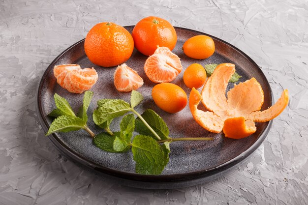 Tangerines, kumquats and a branch of mint on ceramic plate on gray 