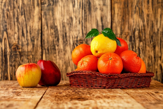 Tangerines and lemon in a wicker basket red apples lie on an old wooden table