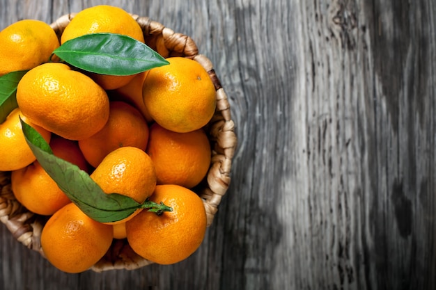 Tangerines with leaves in basket on rustic wooden background