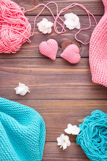 Tangles of pink and mint yarn, snuds and knitting hearts on a wooden table.