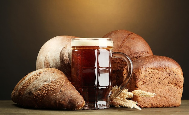 Tankard of kvass and rye breads with ears on wooden table on brown background