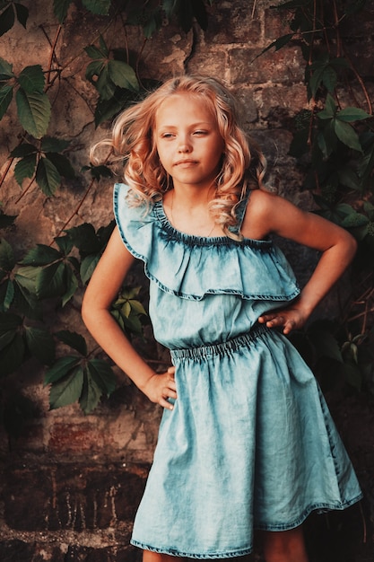 Tanned blonde girl with curly hair posing against the wall with wild grape leaves. High quality photo