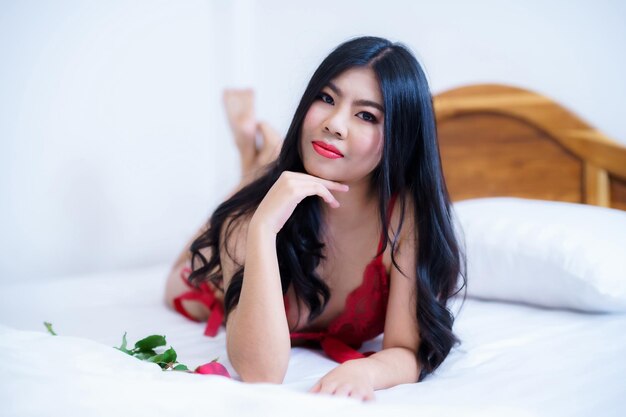 Tanned woman's bodyThailand Asian sexy young woman model in sexy red lingerie holding a red rose posing on the bed in the bedroom valentine's day concept