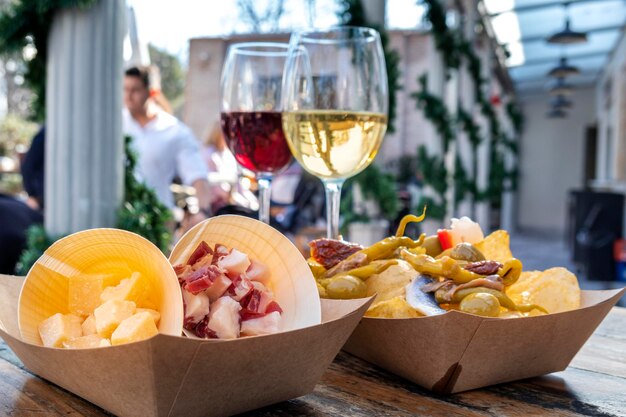 Photo tapas bar cheese ham and pinchos with peppers with glasses of red and white wine on a wooden table in an outdoors cafe