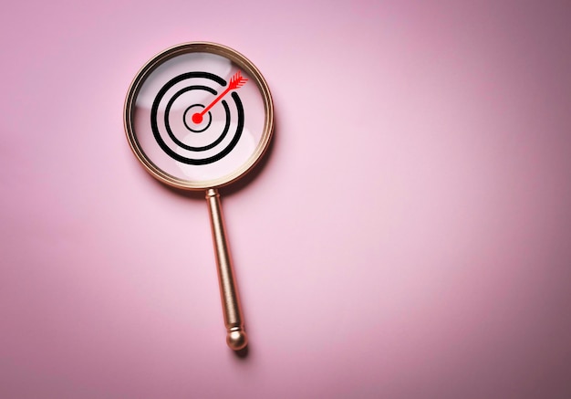 Target board inside of magnifier glass for focus business objective target search concept and success on pink background and copy space