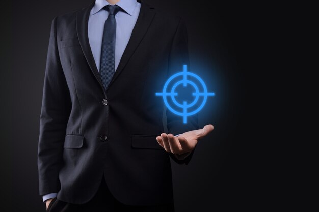 Targeting concept with businessman hand holding target symbol dartboard sketch on chalkboard. Objective target and investment goal concept.