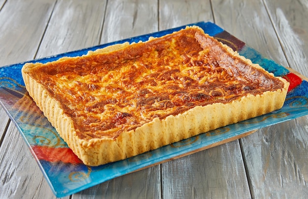 Tart with potatoes and cheese on glass plate on wooden background