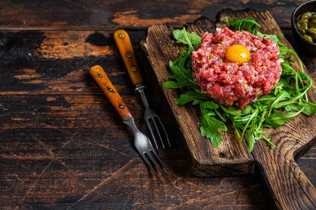 Tartar beef with a quail egg and arugula served on a cutting board.