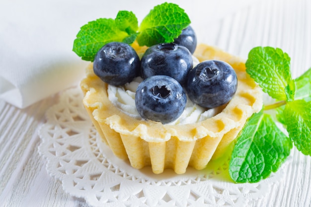 Tartlet with fresh blueberries and cream cheese on white wooden background.