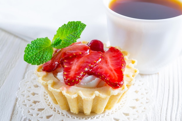 Tartlet with fresh strawberries and cream cheese, and a cup of tea and small cookies.