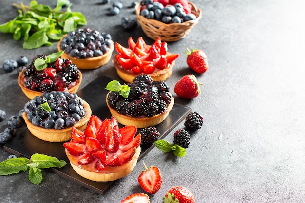 Tartlets with curd cream and fresh berries of strawberries, blueberries, blackberries. Summer fruit baking. Top view. Copy space.