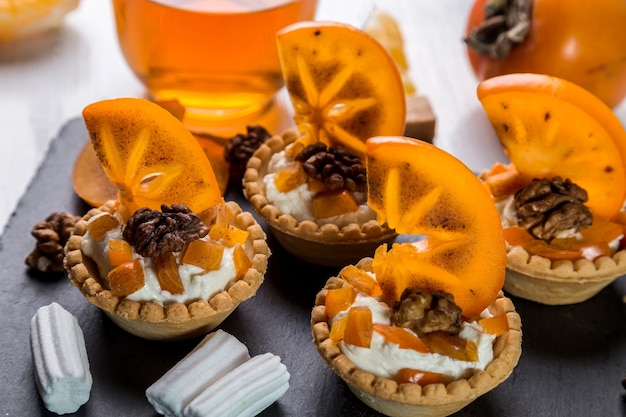 Tartlets with curd cream, persimmon and tea in a transparent cup.