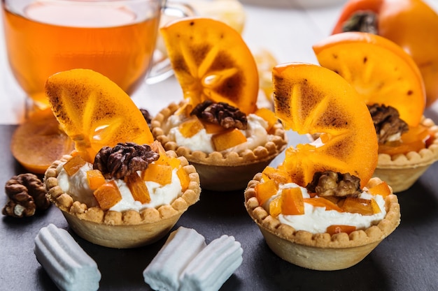 Tartlets with curd cream, persimmon and tea in a transparent cup.