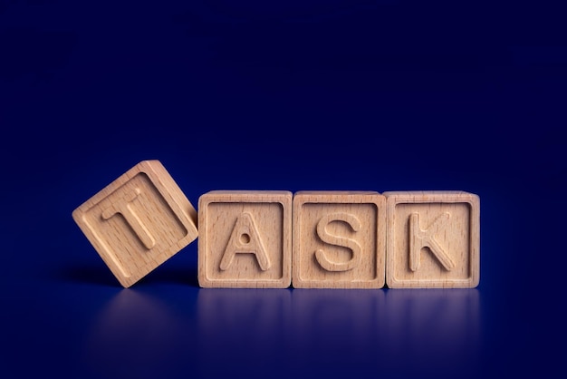 TASK the word on wooden cubes with wooden hand on blue background Business and finance concept