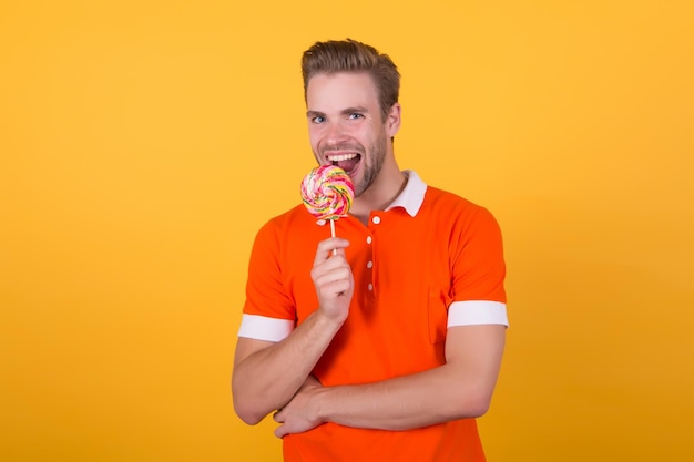 Taste of childhood Happy eating sweets Symbol of happiness Man eat lollipop Man smiling hold lollipop Holiday concept Sugar harmful for health Guy lollipop candy yellow background Sweet boy