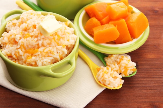 Taste rice porridge with pumpkin in saucepans on wooden background