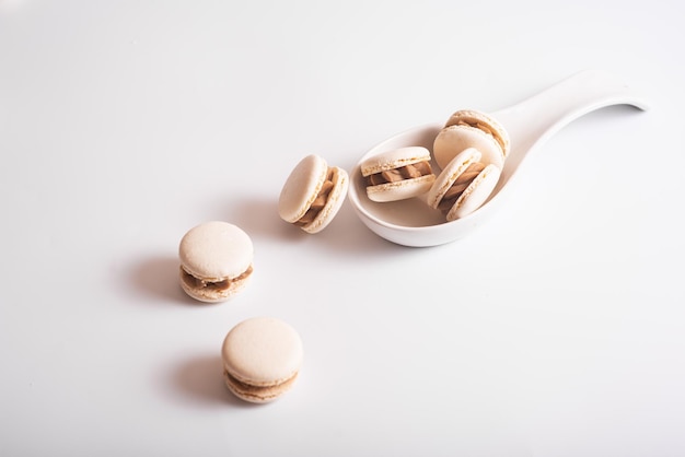 Tasty almond macarons in ceramic white spoon on white background Copy space