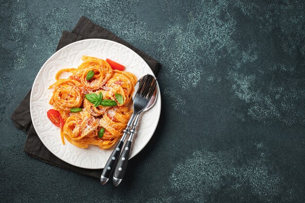 Tasty appetizing classic italian tagliatelle pasta with tomato sauce, cheese parmesan and basil on plate on dark table. View from above, horizontal. Top view with copy space.