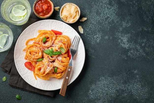 Tasty appetizing classic italian tagliatelle pasta with tomato sauce, cheese parmesan and basil on plate on dark table. View from above, horizontal. Top view with copy space