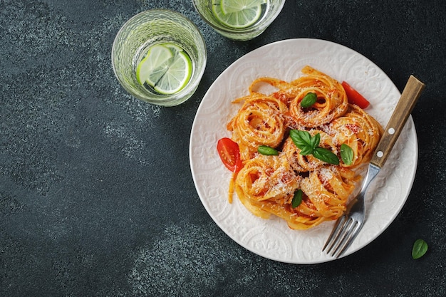 Tasty appetizing classic italian tagliatelle pasta with tomato sauce cheese parmesan and basil on plate on dark table View from above horizontal Top view with copy space