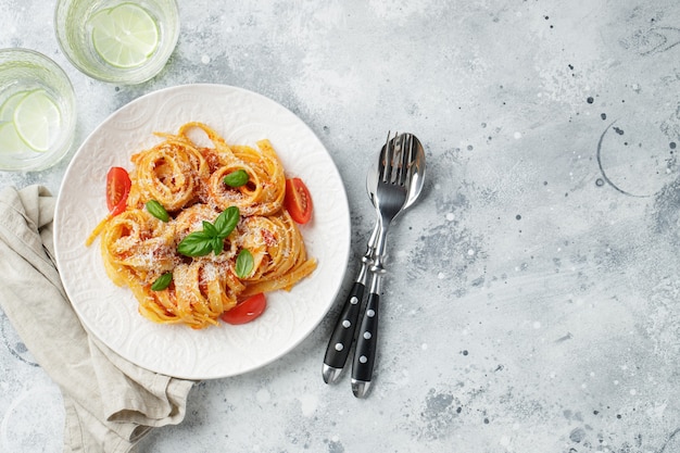 Tasty appetizing classic italian tagliatelle pasta with tomato sauce, cheese parmesan and basil on plate on light table. View from above, horizontal. Top view with copy space.