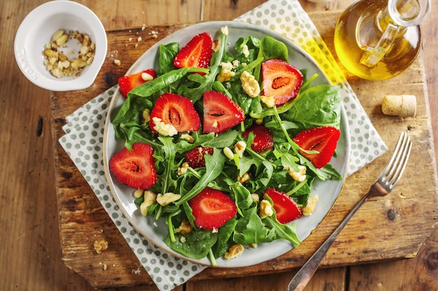 Tasty appetizing freshmade summer salad with arugula, strawberry and nuts served on plate. Closeup