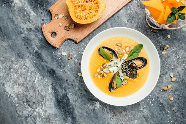 Tasty appetizing pumpkin creamy soup with seafood, mussels, shrimps, blue cheese, mold in a white bowl. banner, menu, recipe place for text, top view