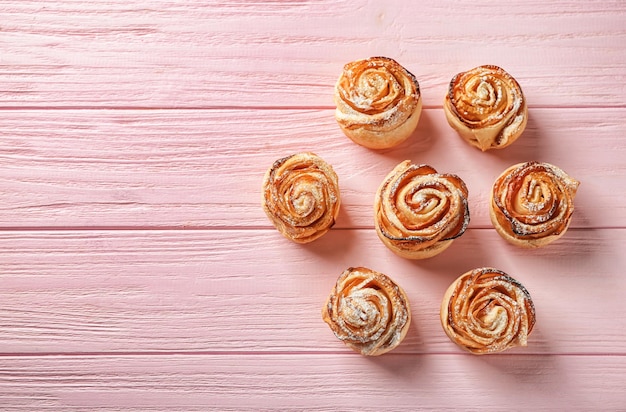 Tasty apple roses from puff pastry on color wooden background