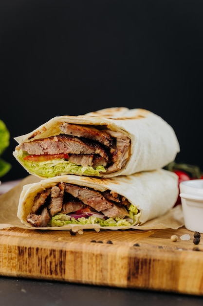 Tasty beef shawarma with fresh salad and vegetables lying on wooden board traditional arab dishes