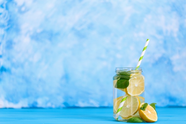 Tasty beverage with lemon and basil in glass jar on blue background