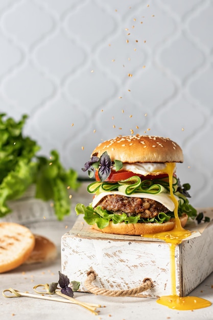 Tasty big burger with leaking egg yolk with a sprinkling of sesame seeds on top on white kitchen tile background