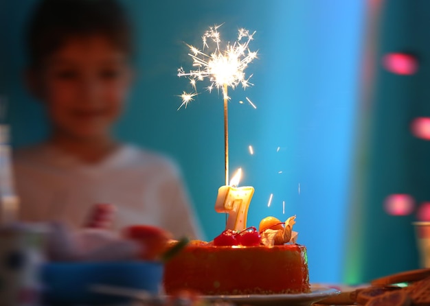 Tasty birthday cake with sparkler and blurred boy on background