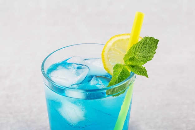 Tasty Blue Lagoon cocktail on light grey table with lemon and mint close up