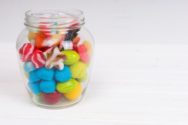 Tasty bright chewing sweets and jelly candies in the glass can on wooden white board