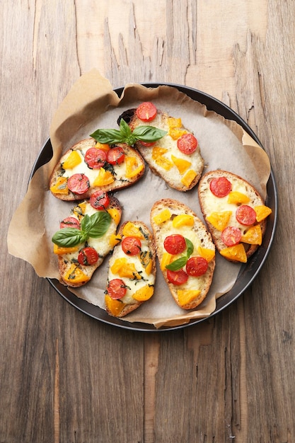 Tasty bruschetta with tomatoes on pan on old wooden table