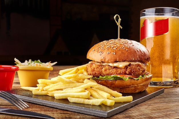 Tasty burger french fries with sauce and glass of beer on black board