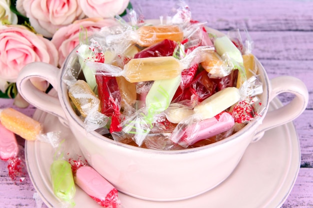 Tasty candies in bowl with flowers on wooden background