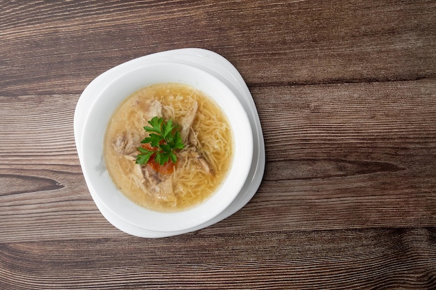 Tasty chicken soup bouillon with noodles chicken meat dill and parsley in a white bowl Isolated on wooden background Healthy meal menu