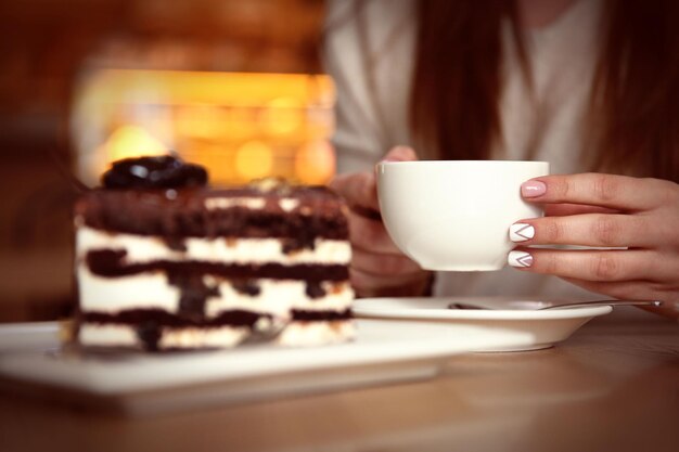 Tasty chocolate cake on table in cafe or restaurant and woman with cup of tea