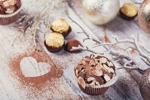 Tasty chocolate cupcake with sweets, heart shaped cocoa powder and winter decoration on white rustic wooden table. Winter holiday background.