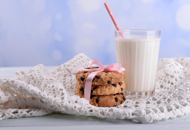 Tasty cookies and glass of milk on color wooden table on bright background